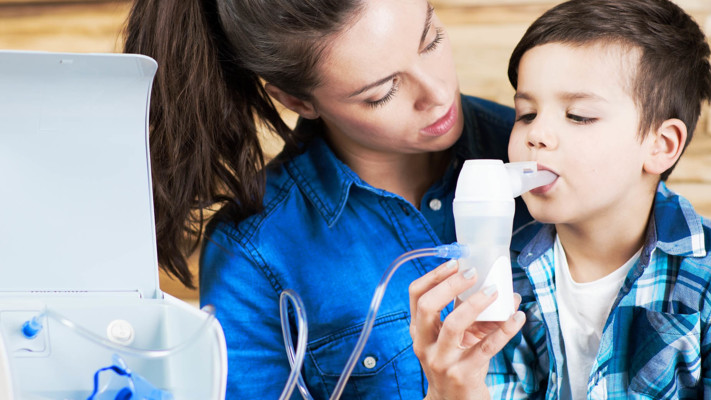 Bé trai bị hen suyễn đang xông khí dung tại nhà dưới sự hướng dẫn của mẹ